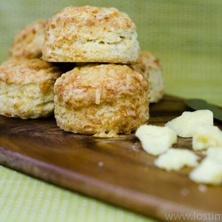 a wooden board with fresh cheese scones and some diced cheese to the foreground all on a lime green backdrop.