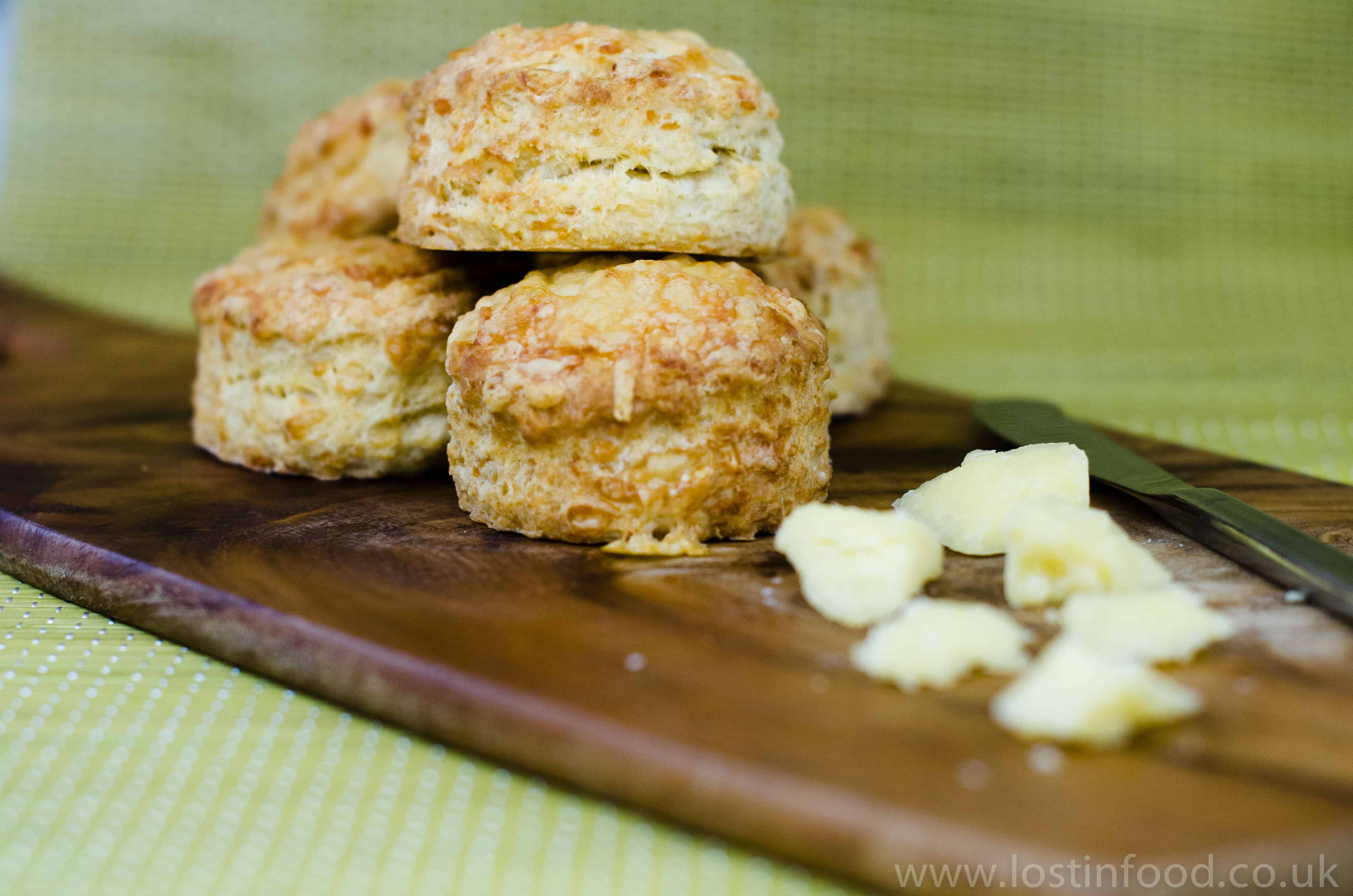 a wooden board with fresh cheese scones and some diced cheese to the foreground all on a lime green backdrop.