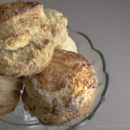A glass cake stand with 4 large buttermilk scones piled together on top.
