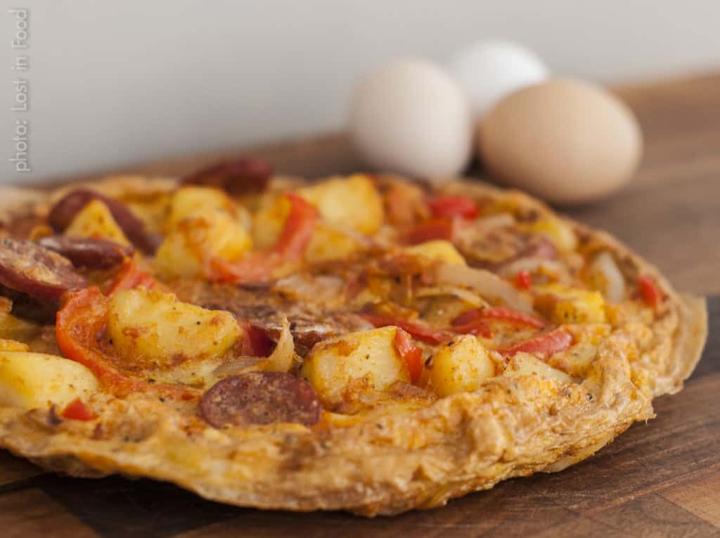 Closeup chorizo tortilla on wooden board with eggs in background