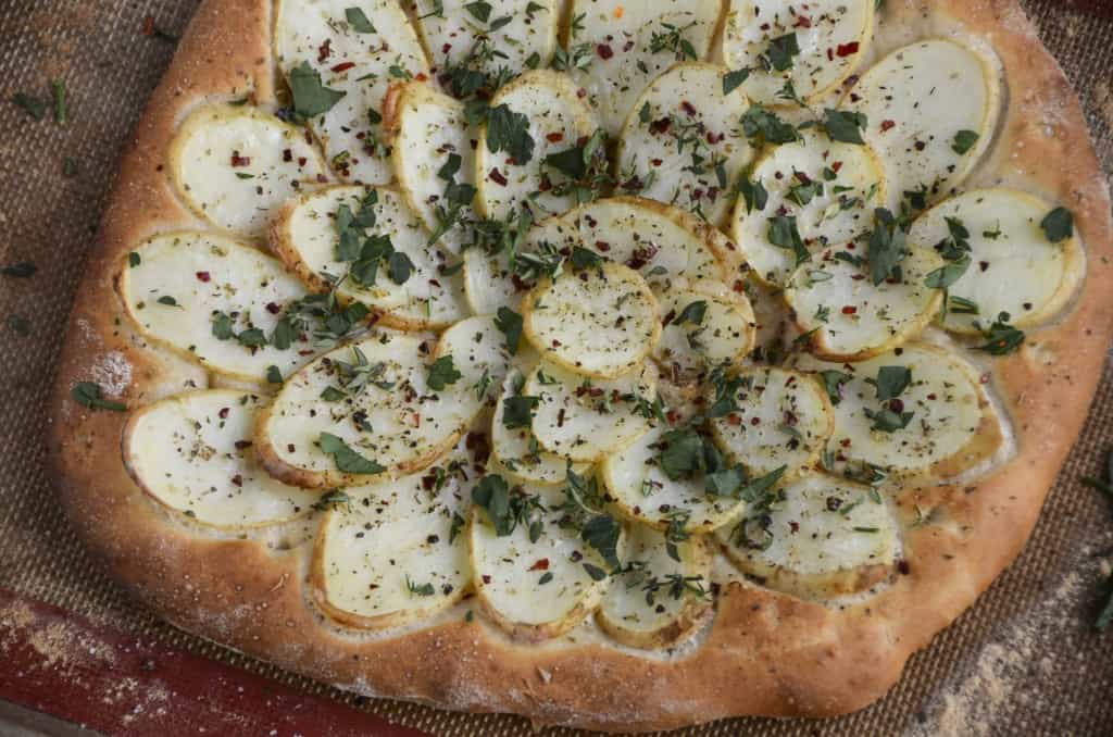 A large potato galette sprinkled with dried herbs fresh from the oven still on a baking tray.