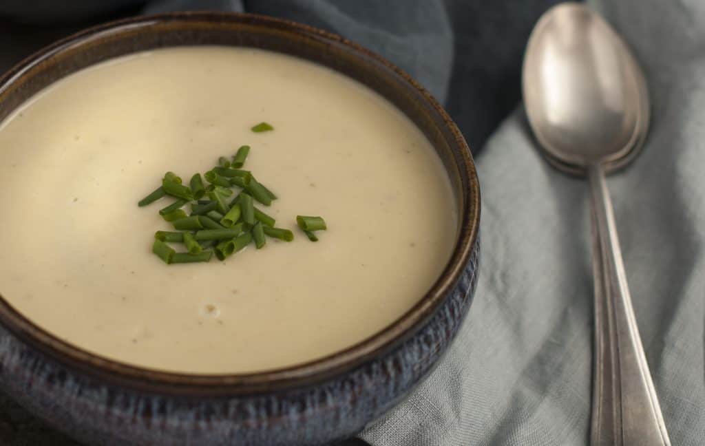 Creamy Jeruselum artichoke soup in a dark blue pottery bowl with a blue napkin and soup spoon to the right