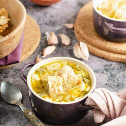 clear garlic soup with sourdough croutons in a le crueset purple dish with a rustic feel