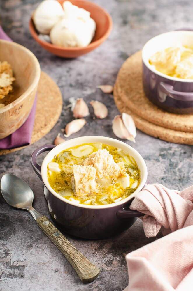 clear garlic soup with sourdough croutons in a le crueset purple dish with a rustic feel