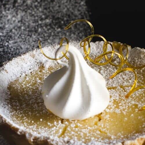 lemon tart on a black plate with sugar spirals and a merengue