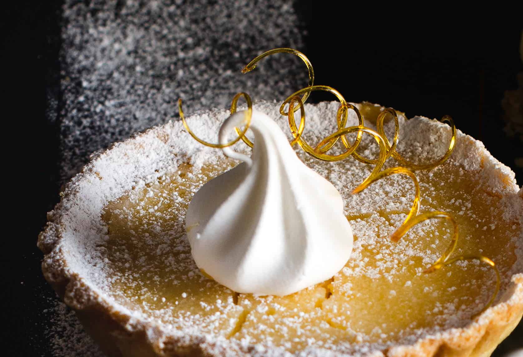 lemon tart with ice cream on a black plate with sugar spirals and a merengue