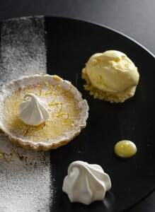 #CookBlogShare image of Lemon tart with meringues and limoncello ice cream on a black plate decorated with icing sugar
