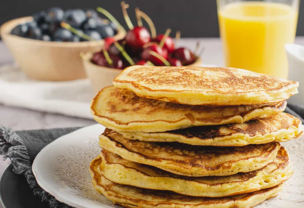 a stack of scotch pancakes, cherries in the back with blueberries and orange jucie