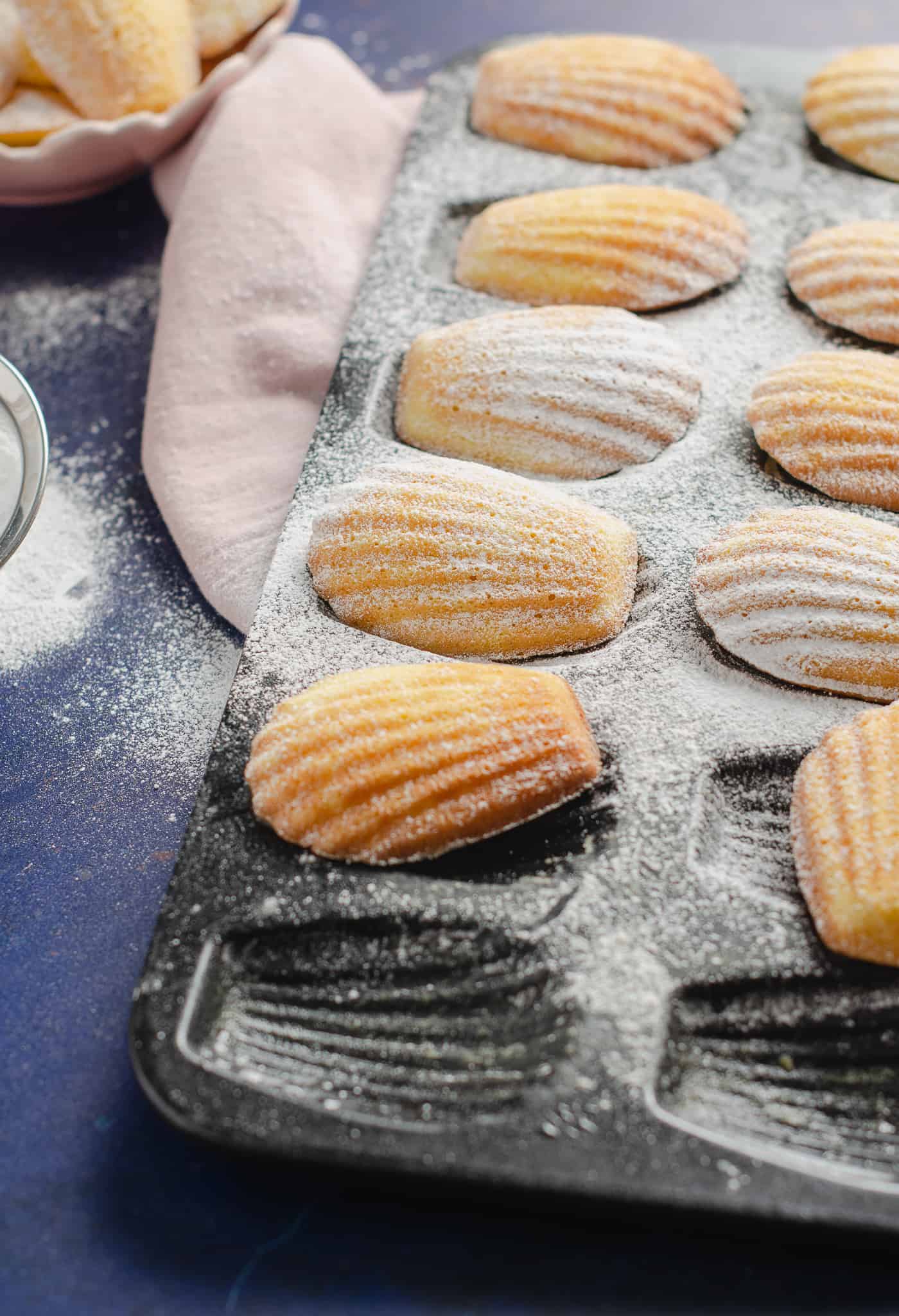 Madeleines in a baking tray dusted with icing sugar with a pink linen napkin