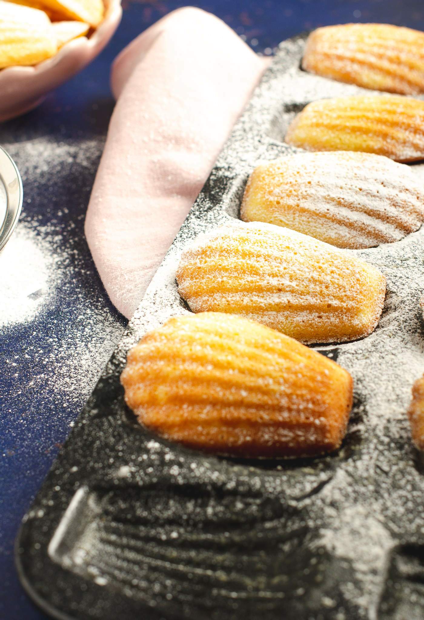 Close up of Madeleines in a black baking tray dusted with icing sugar