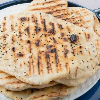 freshly cooked flatbreads piled on top of a white plate served on a blue ceramic tray