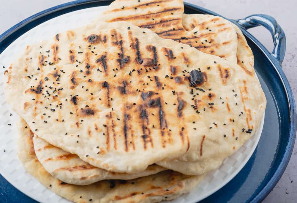 freshly cooked flatbreads piled on top of a white plate served on a blue ceramic tray