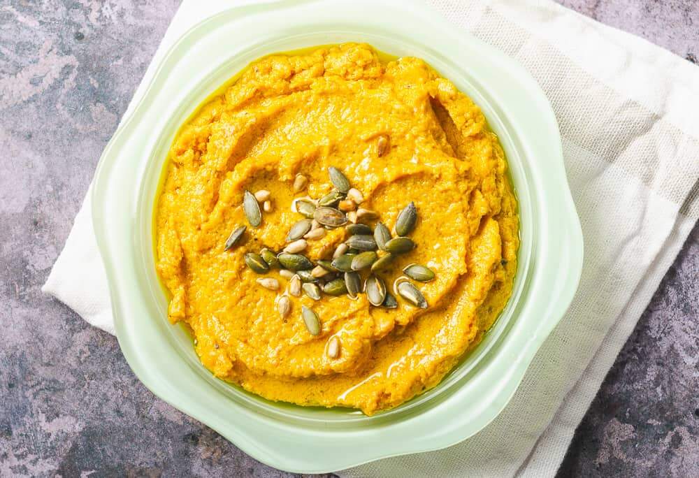 close up shot of carrot hummus in a green bowl sprinkled with toasted seeds