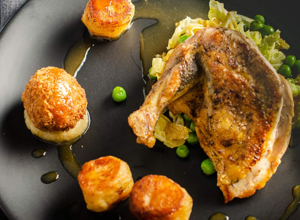 A plate of guinea fowl supreme, fondant potatoes, chicken jus with a chicken leg bonbon, onion puree and pan fried greens