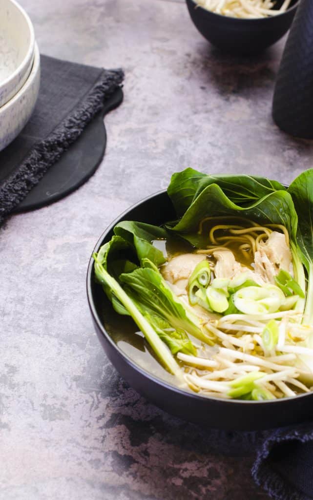 Asian style chicken broth with pak choi and bean sprouts served in a black bowl