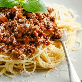 A close up of a large plate of spaghetti bolognese with a fork ready to eat and topped with basil