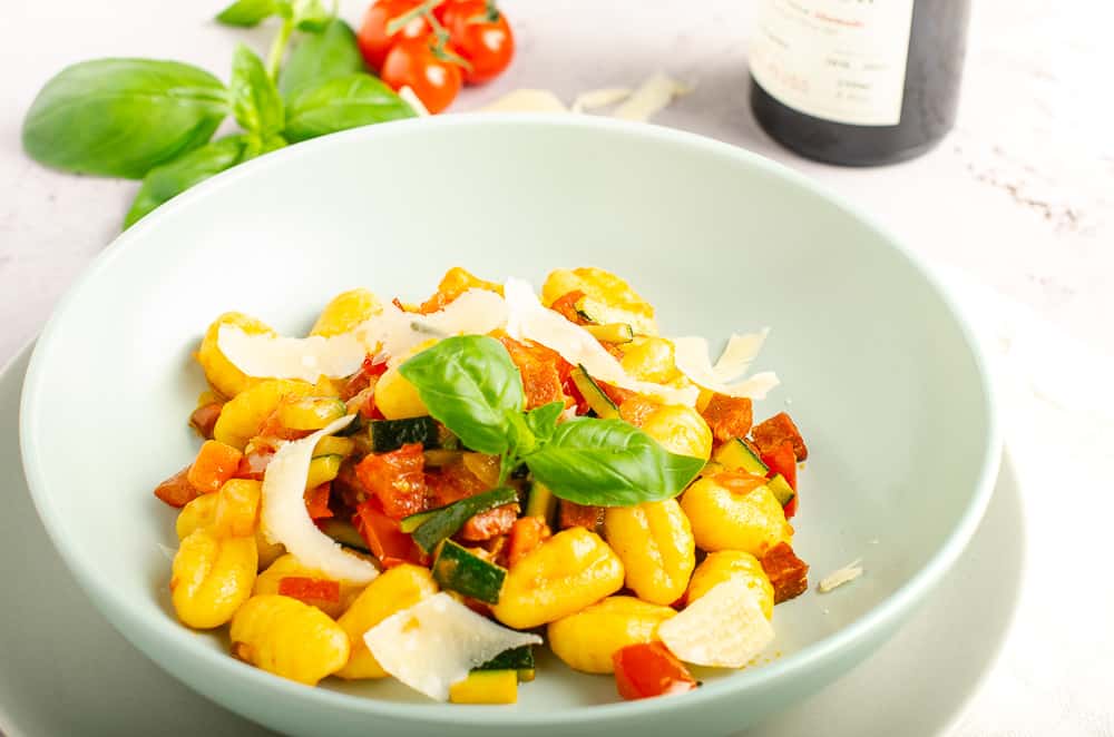 A bowl of gnocchi with fresh tomatoes, courgettes, chorizo and topped with parmesan and basil.