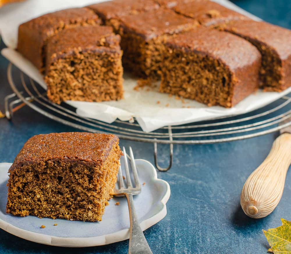 Yorkshire Parkin, a single slice to the front on a small blue plate and the remainder to the back slightly blurred all on a blue backdrop.