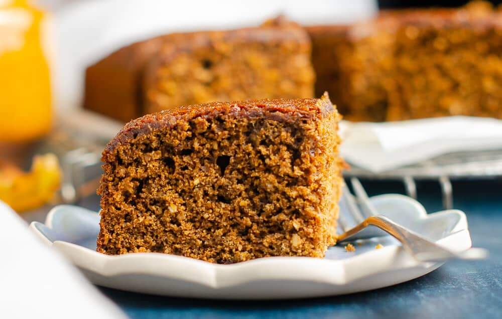 A close up view of a piece of yorkshire parkin with a crumbly texture on a scalloped edge plate and a blurred background.