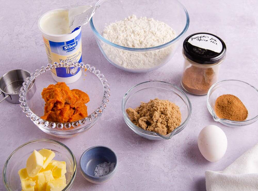 Ingredients laid out to make pumpkin spice scones, including flour, salt, brown sugar, egg, pumpkin spice and buttermilk and cold cubed butter.