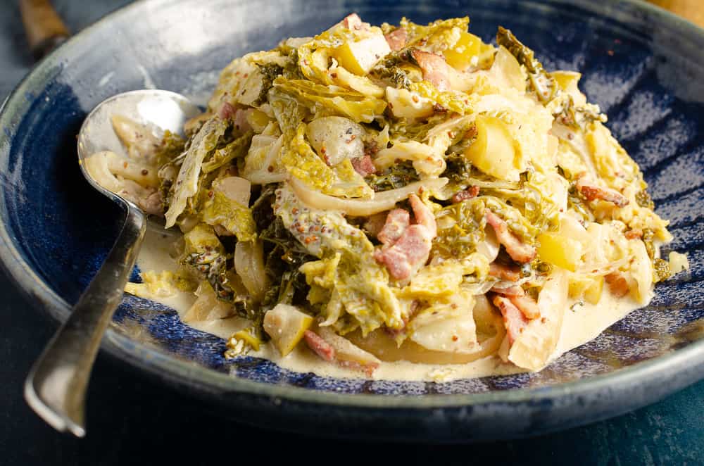 A large blue pottery serving bowl filled with cabbage cooked with apples, bacon, cider and mustard.