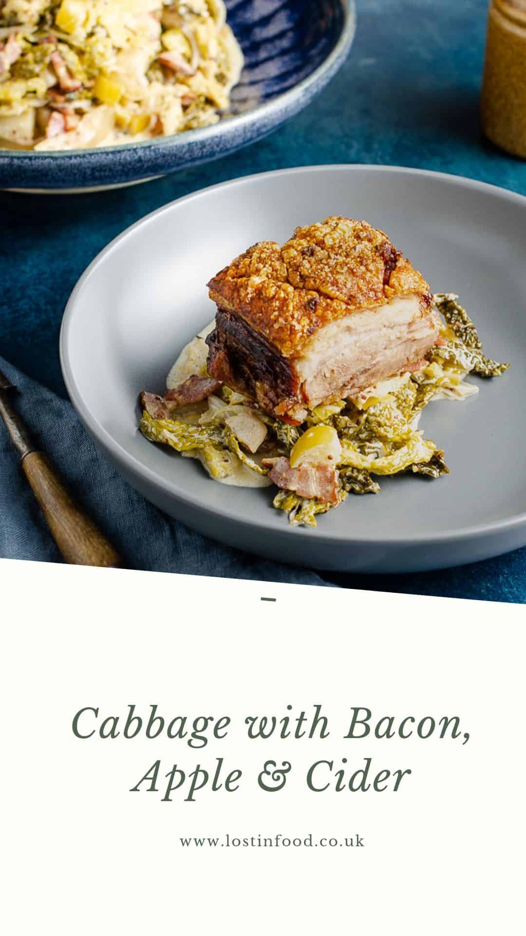 Cabbage with apple, bacon and cider served under a roasted piece of pork belly on a grey bowl and a wooden handle fork to the side and a large bowl of the cabbage dish to the back.