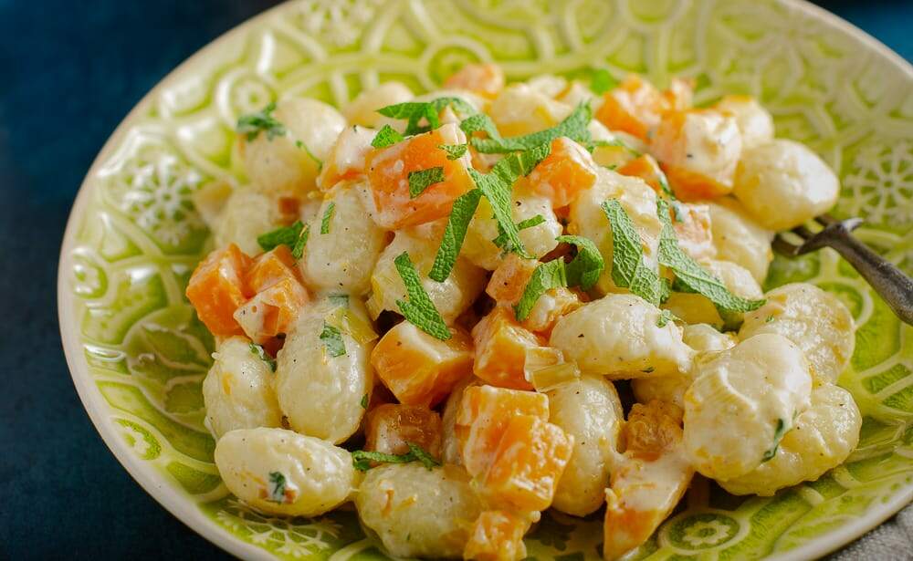 A close up shot of a dish of pumpkin gnocchi with sage scattered through it and served on a patterned green plate.