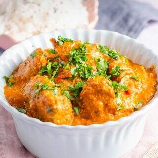 A delicious bowl of butter chicken in a pale blue bowl sat on a pink napkin with a bowl of rice to the back.