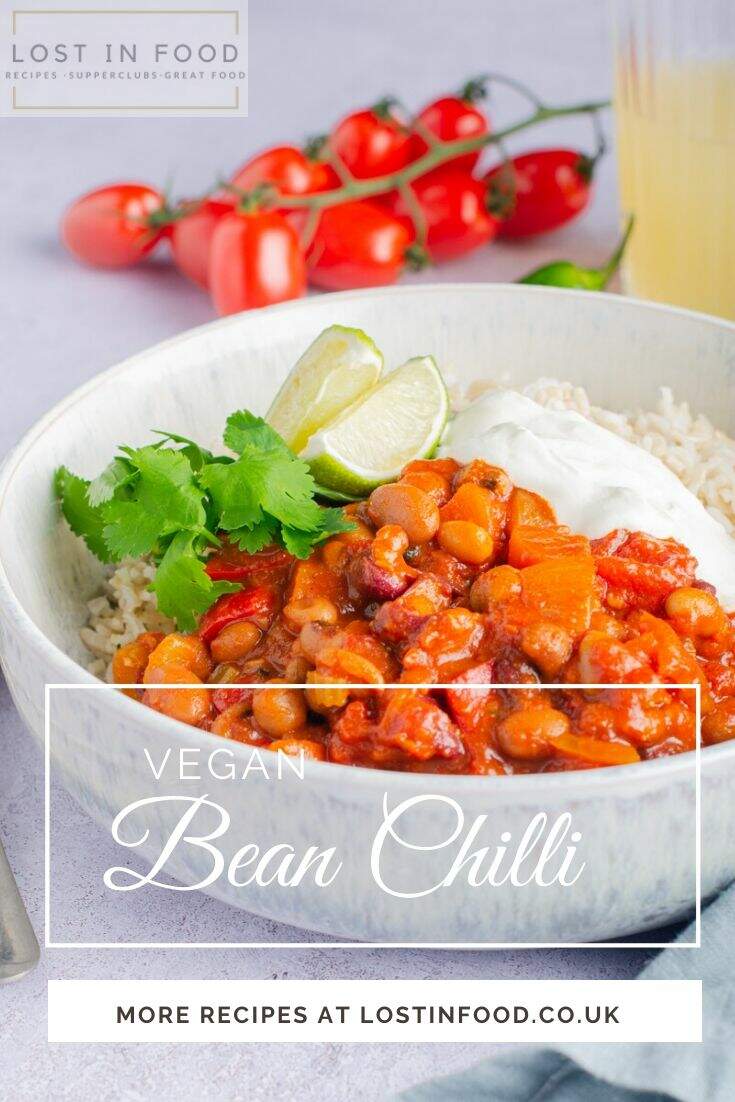 A bowl of vegan bean chilli with basmati rice and topped with sour cream. Some vine tomatoes to the back and with text overlaid naming the dish