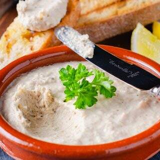 a closeup view of a dish of smoked mackerel pate garnished with parsley and sitting o a blue napkin with a bone handle knife taking a first dip.