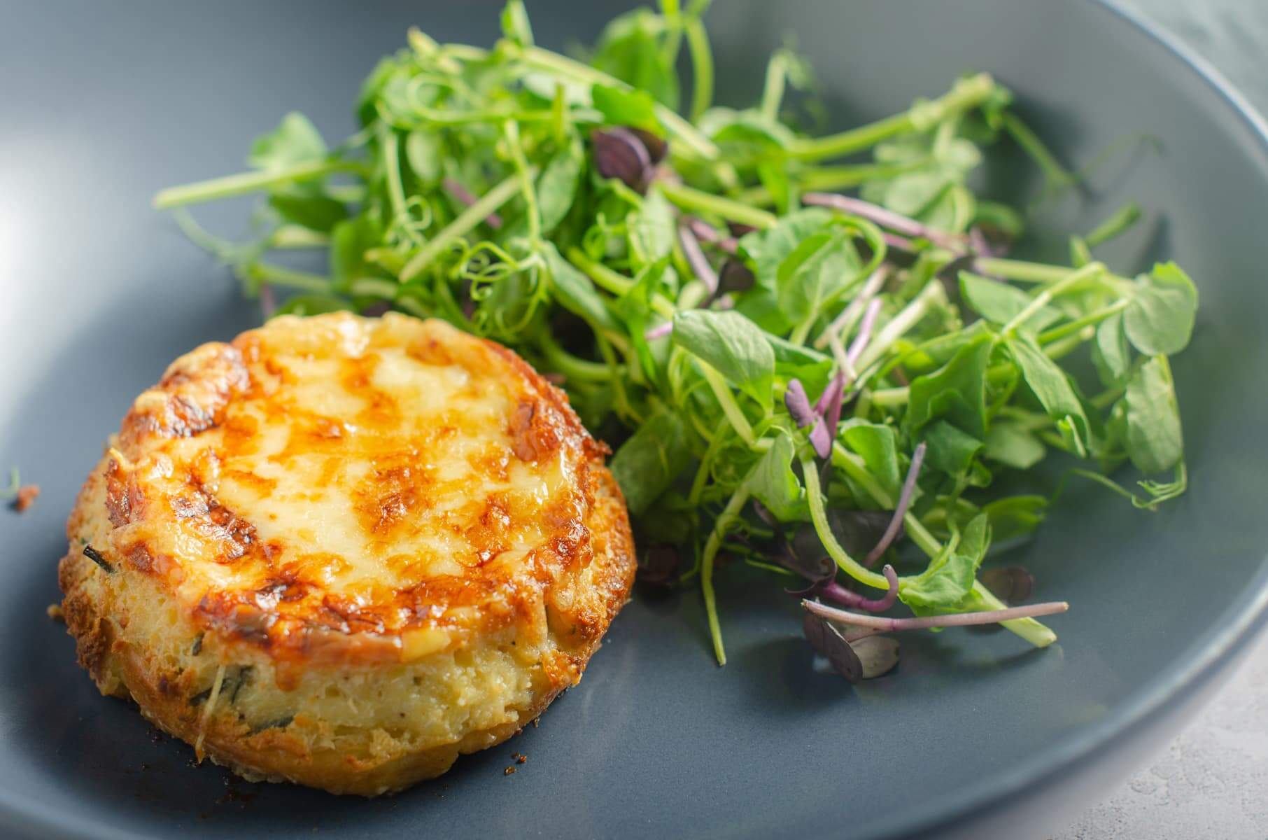 A twice baked cheese souffle fresh from the oven served on a dark blue plate with a green salad.