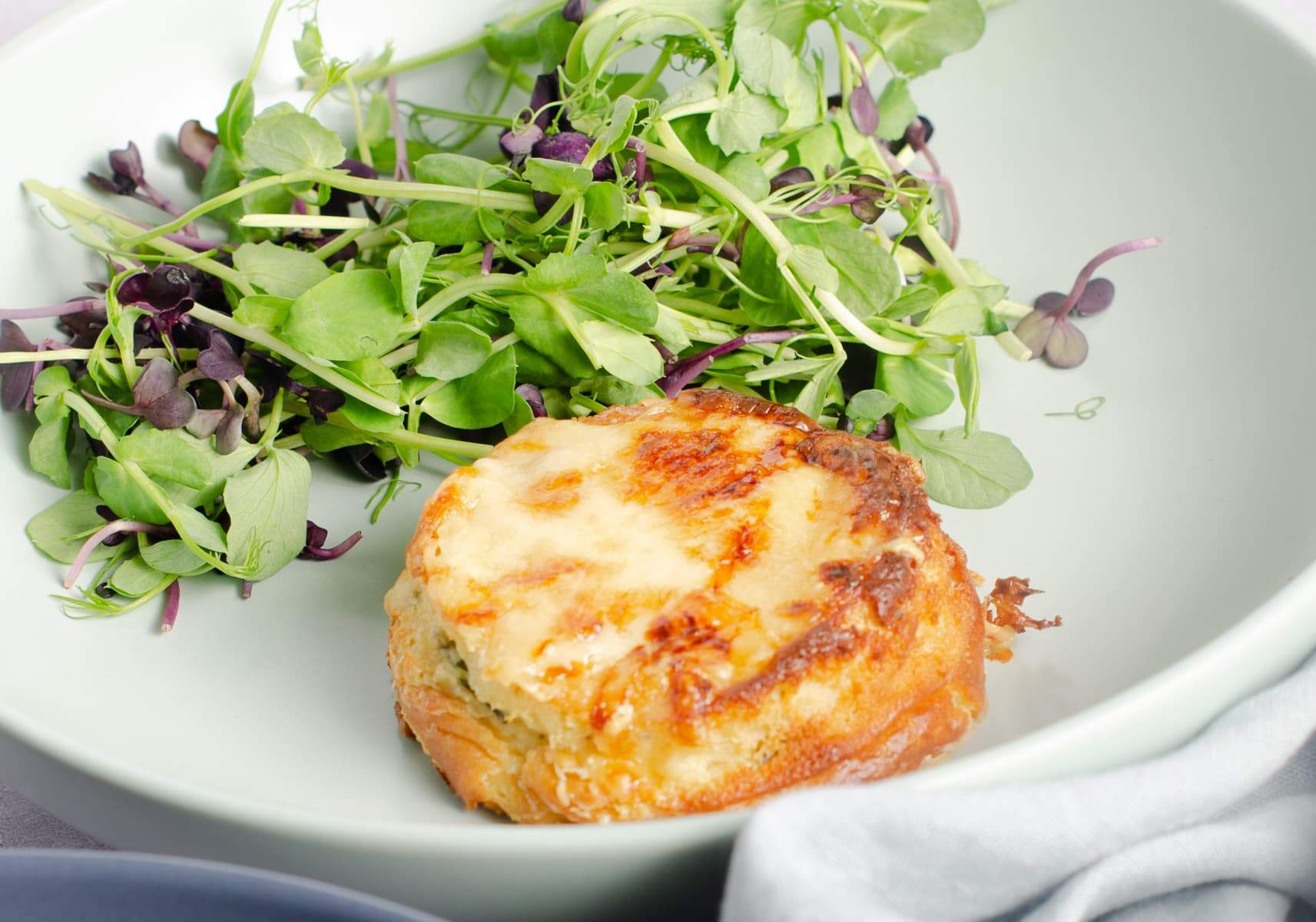 A twice baked cheese souffle fresh from the oven served on a pale green plate with a green salad.