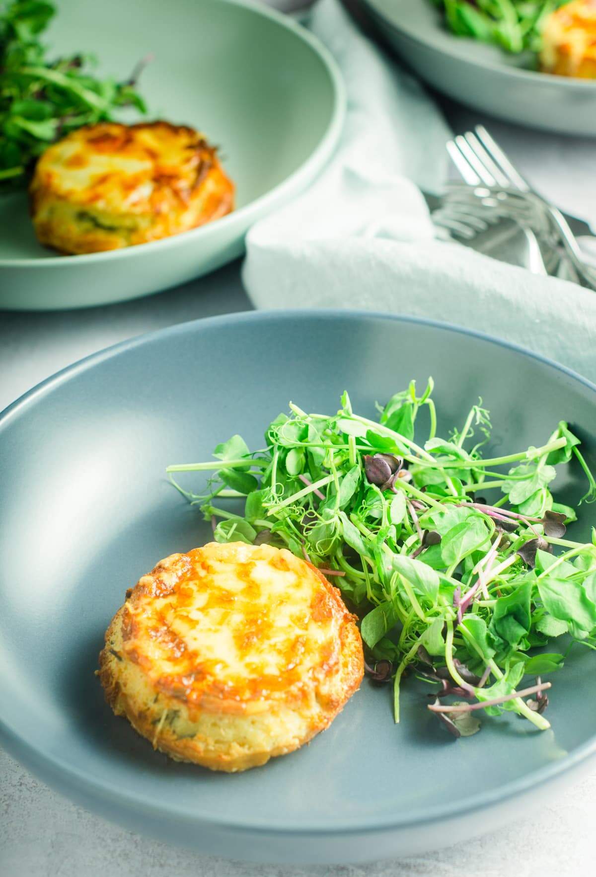 A table setting of 3 plates serving twice baked cheese souffles with side green salad.