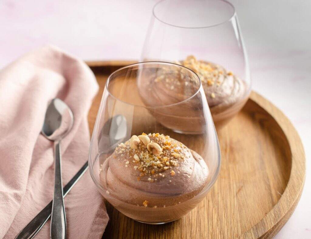 a frontal view of 2 glasses filled with a creamy nutella mousse and garnished with praline crumbs