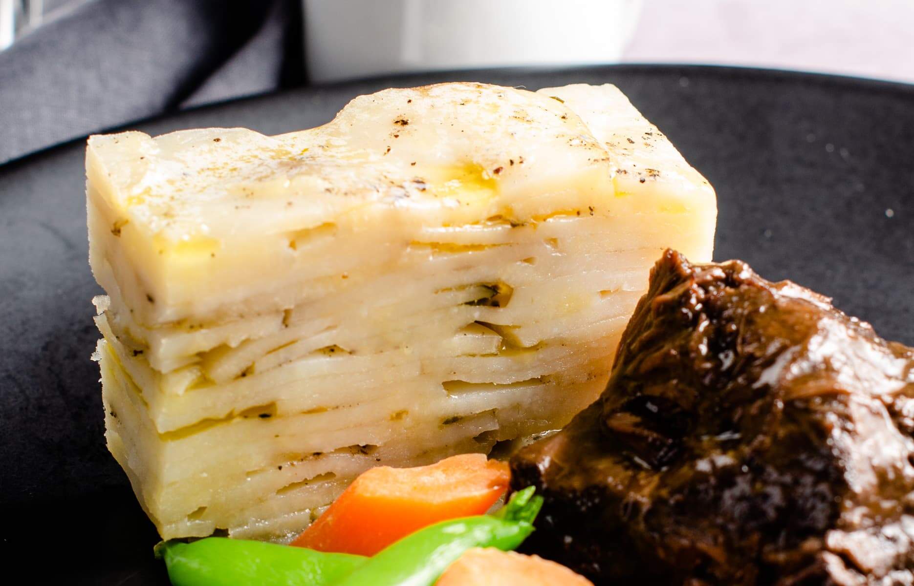 Pave potatoes up close to show all the layers in the potato dish, served with beef cheek stew and vegetables.