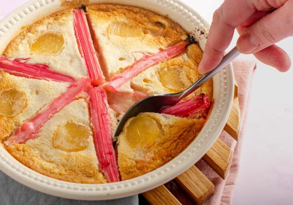 Rhubarb clafoutis with stem ginger, a deliciously light dessert with a hand digging into the dessert with a spoon.