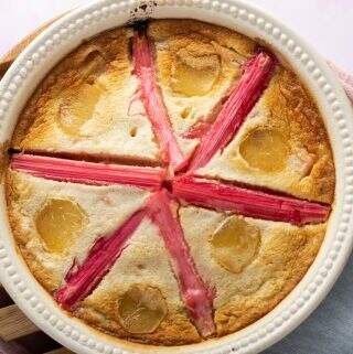 Rhubarb clafoutis with stem ginger, a deliciously light dessert sitting on a wooden trivet and decorated with a star shaped pattern with stems of poached pink rhubarb.