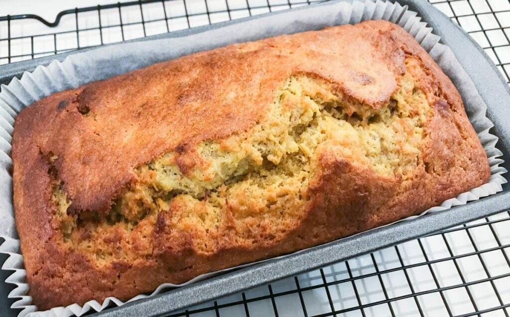 A baked banana loaf or bread straight from the oven still sitting in the loaf tin on top of a wire cooling rack.