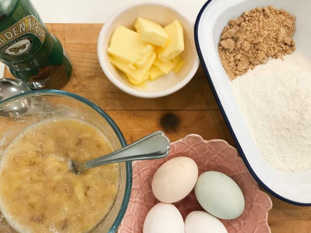 Ingredients for banana bread, mashed bananas, eggs, golden syrup, butter, flour and brown sugar.