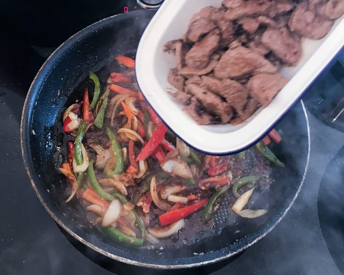 Returning seared beef to the stir fried vegetables for the beef & black bean dish in a hot fry pan.