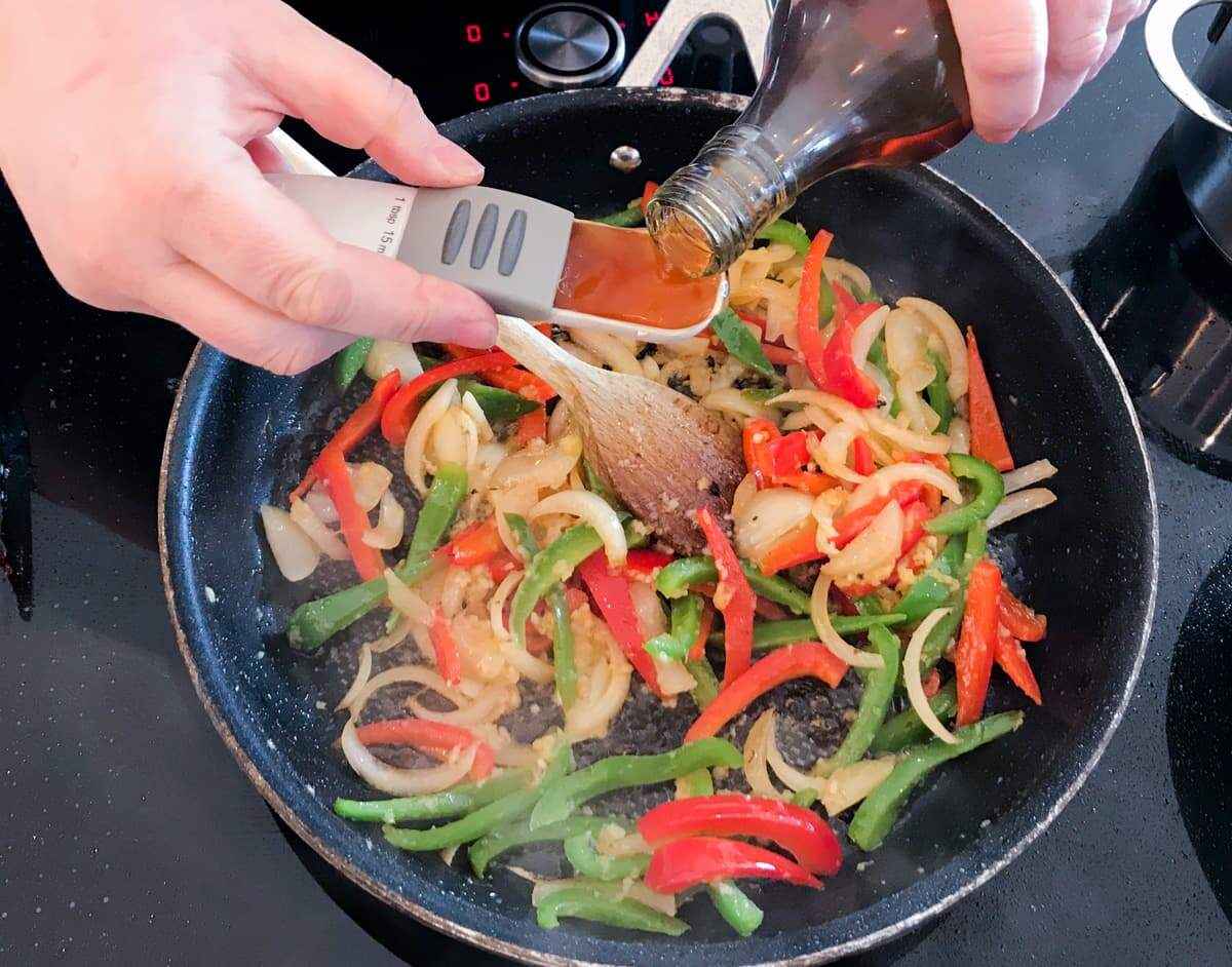 Adding shaoxing rice wine to stir fried peppers, onion, garlic, chilli and garlic.