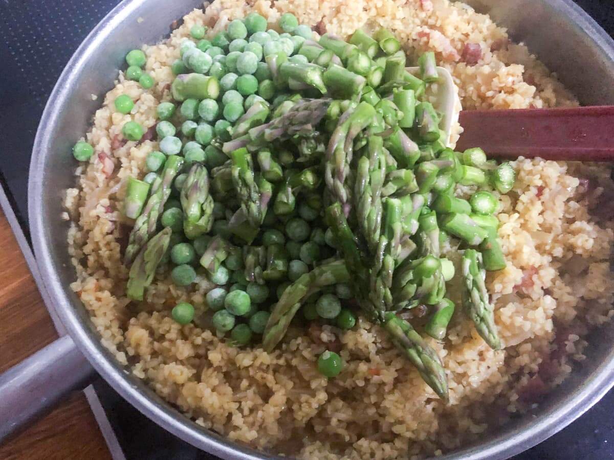 Adding frozen peas and chopped asparagus to a bulgar wheat risotto.