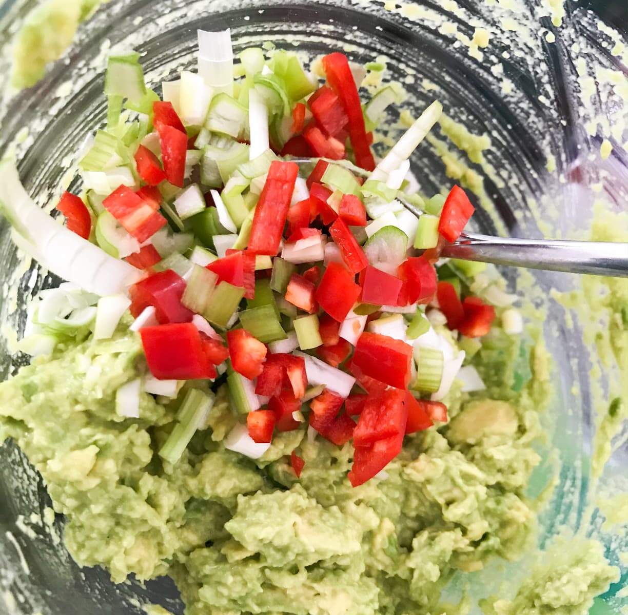 Smashed avocado with finely diced chillies and spring onions being add to make guacamole.
