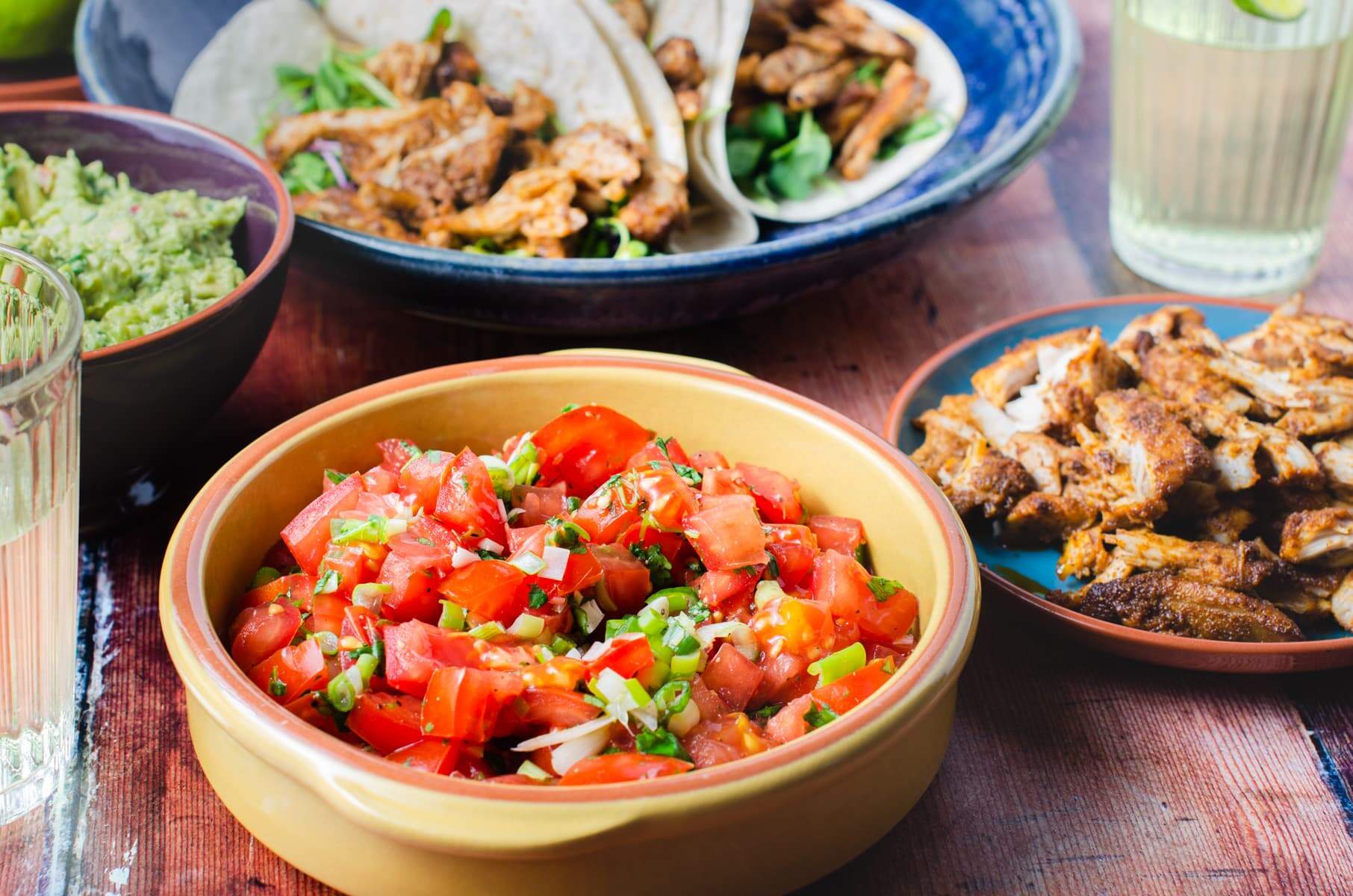 All the makings of a chicken taco party, fresh tomato salsa, cooked chicken, guacamole and lime decorated drinks.