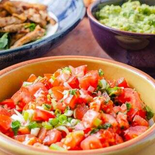 Easy no cook fresh tomato salsa in a yellow bowl with guacamole and chicken to the back perfect for a taco night.