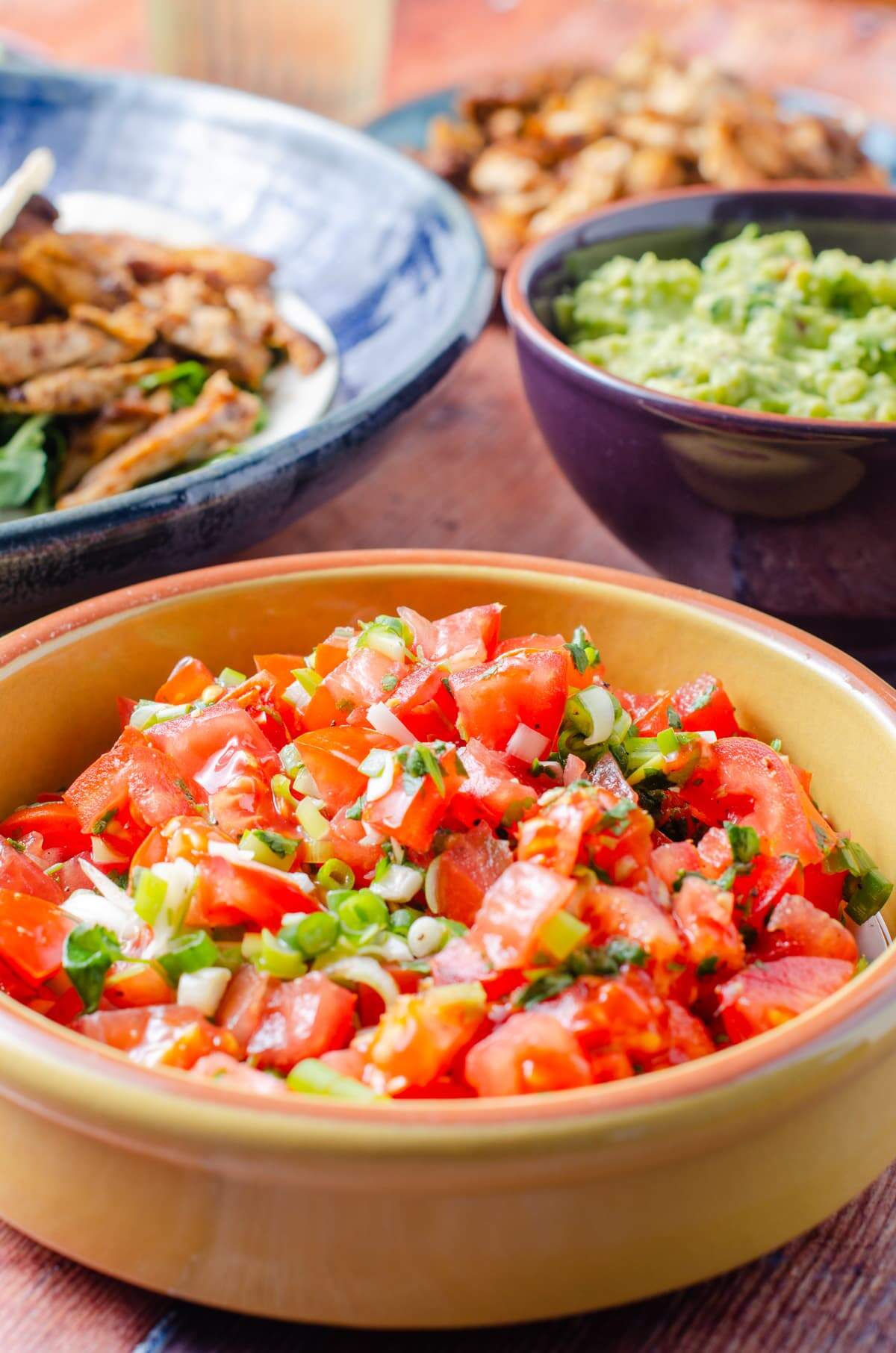 Easy no cook fresh tomato salsa in a yellow bowl with guacamole and chicken to the back perfect for a taco night.