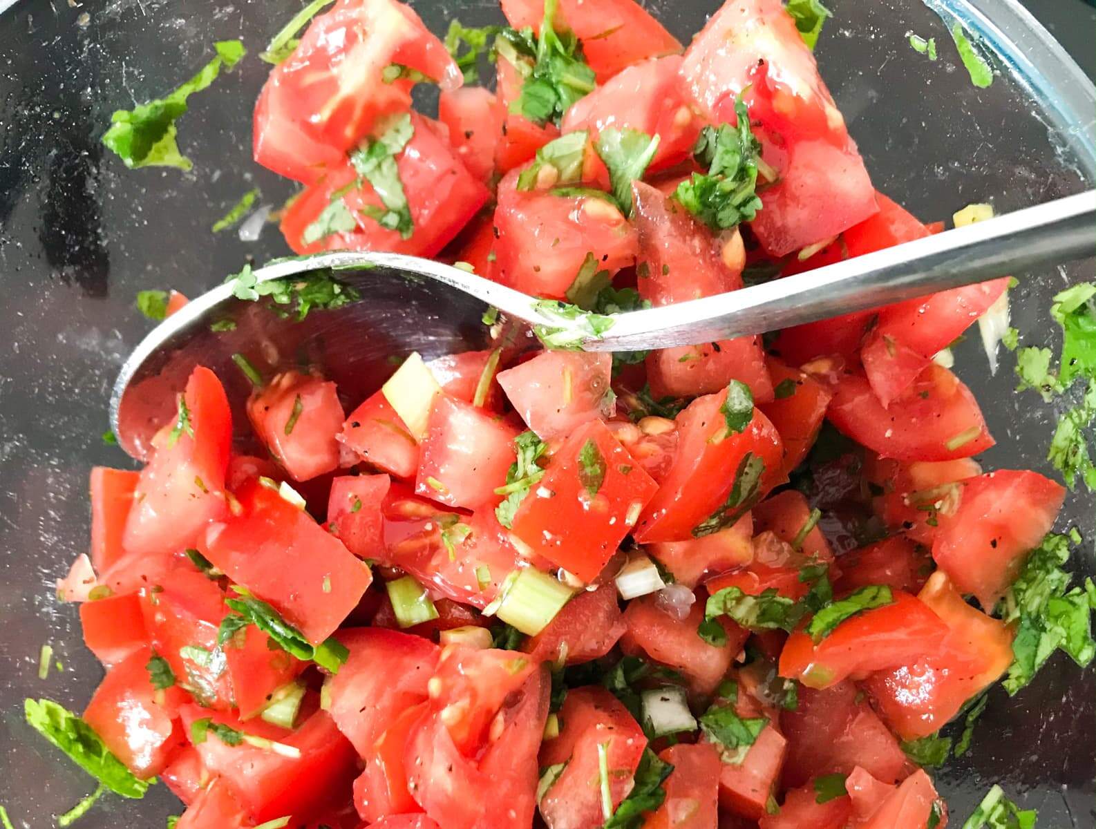 Mixing the fresh chopped tomatoes, spring onions and herbs in a bowl to finish off the tomato salsa.