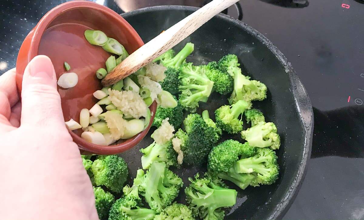 Stir frying broccoli in a hot pan and adding chopped spring onions, grated ginger and garlic.