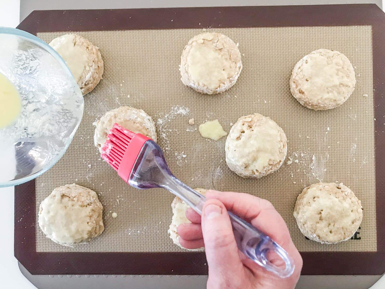 A hand brushing the top of scones with leftover buttermilk and egg mix to glaze the top of scones before baking.
