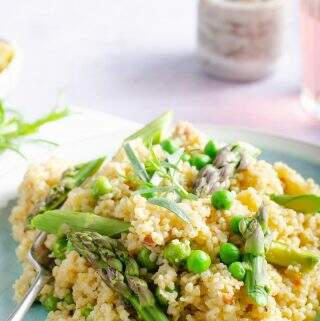 A blue marbled plate with bulgar wheat risotto with peas and asparagus, a glass of rose to the back a marbled pinch pot of salt sat on a white waffled napkin.